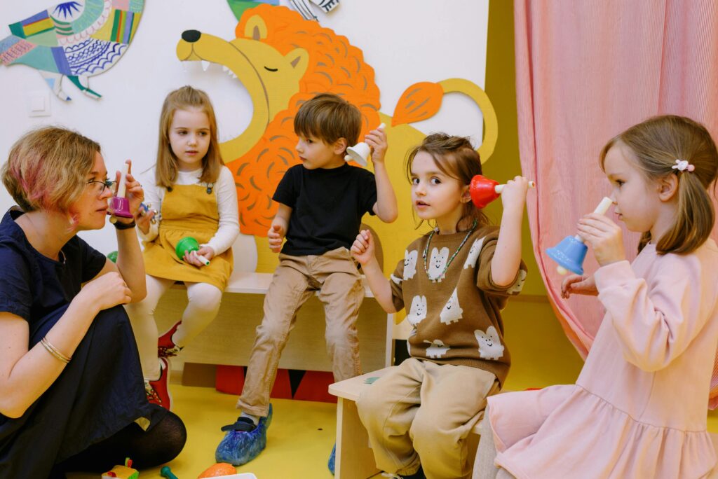 pexels-photo-8535230-8535230 Young children playing musical bells in a colorful classroom setting with a teacher.